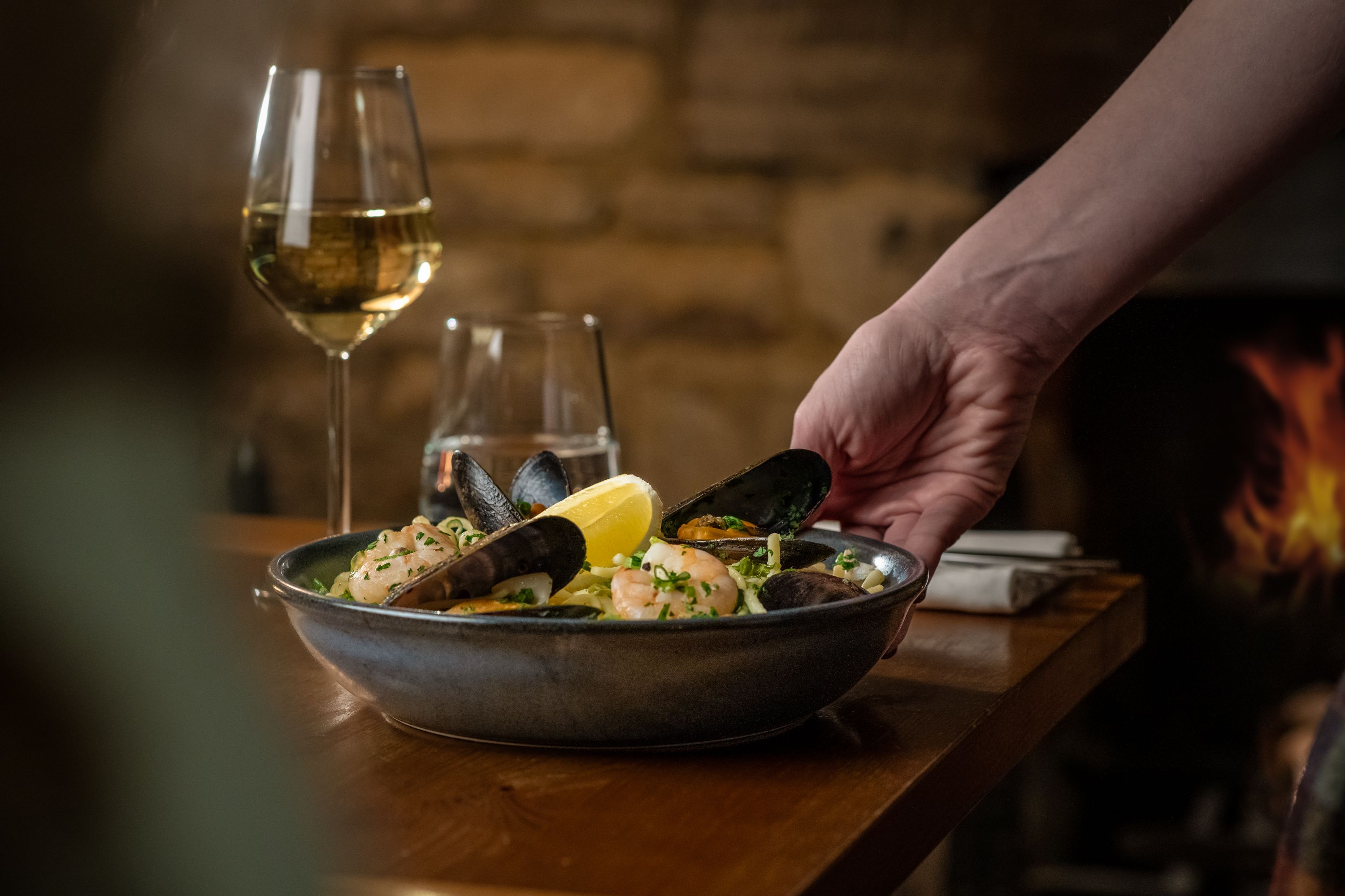 a waitress placing a plate of seafood with white wine